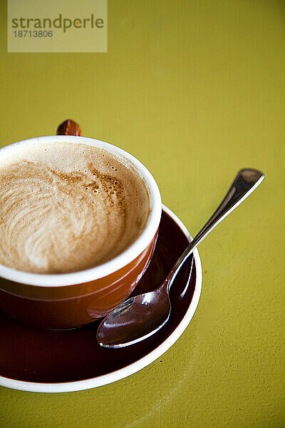 Ein Latte in einer Kaffeetasse auf einem bunten Tisch.