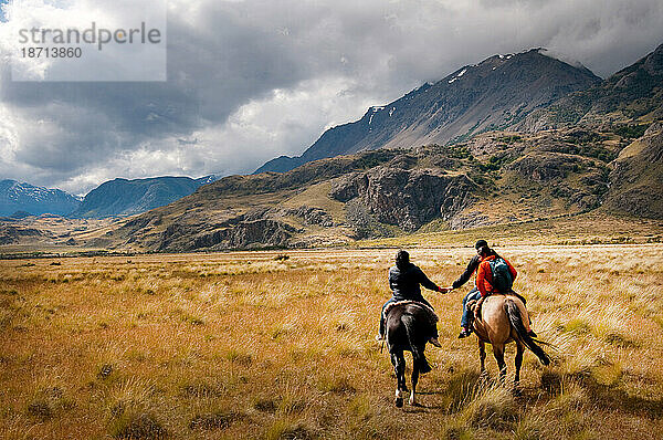 Ein Weibchen und ein Weibchen halten sich auf dem Rücken ihres Pferdes an den Händen  während sie sich auf den Weg machen  um Schafe auf der Estancia Chacabuco in Patagonien zu hüten.
