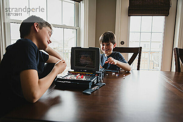 Jungen lachen  während sie gemeinsam am Tisch ein Brettspiel spielen.