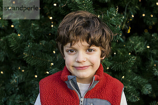 Porträt eines glücklichen  lockigen Jungen vor einem Weihnachtsbaum