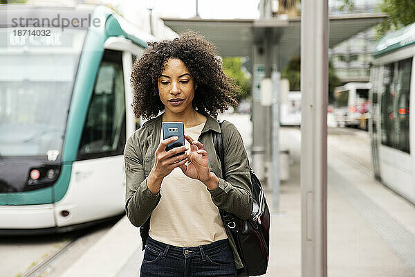 Schöne entspannte Frau  die mit seinem Telefon auf einem Straßenbahnsteig eine SMS schreibt.