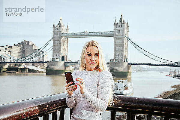 Attraktive Frau mit Mobiltelefon und Blick auf den Hintergrund der Tower Bridge