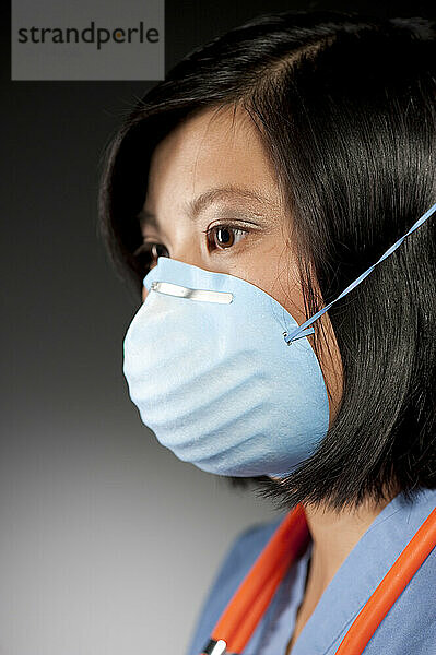 Studioporträt einer 21-jährigen asiatischen Frau  die eine Schutzmaske trägt.