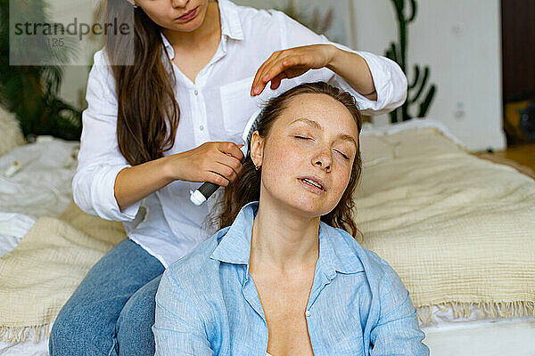 Zwei junge Frauen sitzen zu Hause zusammen  eine bürstet einer anderen die Haare