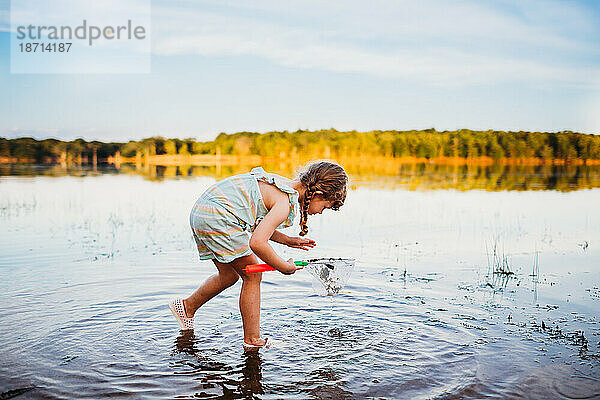 Junges Mädchen bückt sich  um Fische im Wasser am See zu sehen