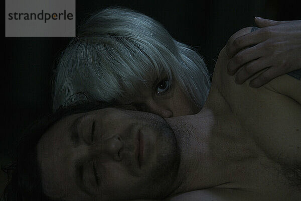 Eine Frau schaut einem Mann auf die Schulter  während sie zusammen im Dunkeln liegen.