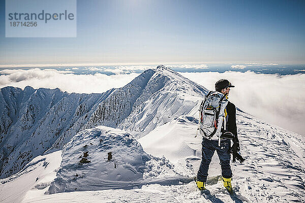 Mann mit Rucksack steht im Winter auf dem schneebedeckten Gipfel von Katahdin  Maine
