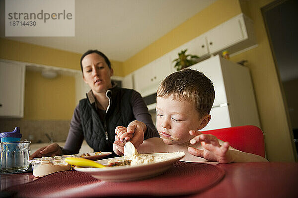Ein kleiner Junge starrt auf seinen Teller und erhält Hilfe von seiner Mutter  während er in Austin  Texas  sein Frühstück isst.
