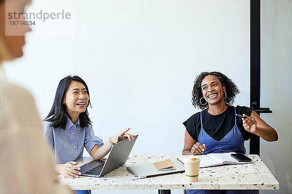 Glückliche Unternehmerinnen sitzen während eines Treffens im Café am Schreibtisch