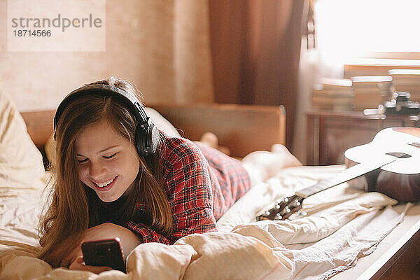 Glücklicher Teenager  der sein Smartphone benutzt  während er über Kopfhörer Musik hört