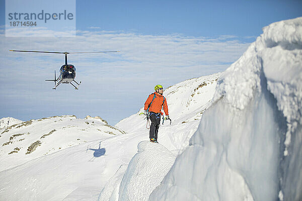 Eiskletterer blickt auf seine nächste Herausforderung  Hubschrauber im Hintergrund.