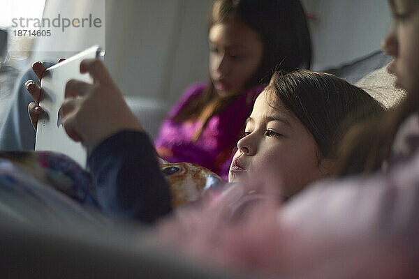 Drei junge asiatische Mädchen spielen zu Hause auf dem Sofa mit ihrem Tablet