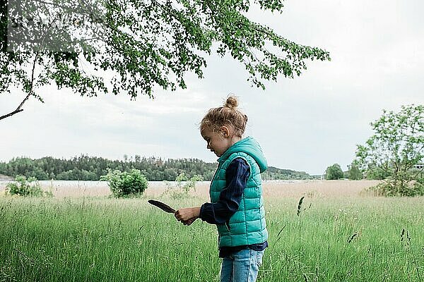 Ein junges Mädchen stand auf einem Feld und hielt eine Feder in der Hand und sah glücklich aus