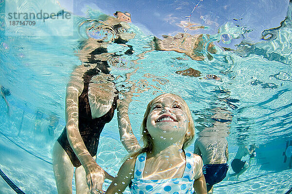 Ein junges Mädchen unter Wasser  während sie mit ihrer Mutter in einem Pool schwimmen lernt.