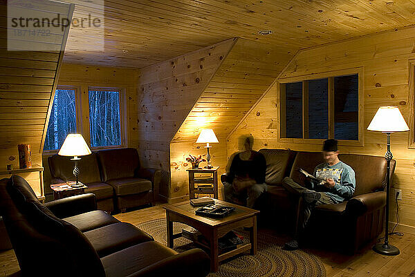 Zwei Männer entspannen sich abends auf einem Ledersofa in der Poplar Stream Hut von Maine Huts and Trails. Maine  Neuengland.