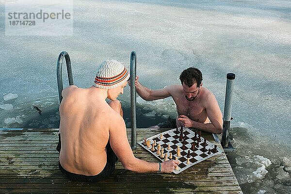 Zwei Männer spielen Schach  während sie in der Ostsee im kalten Wasser schwimmen