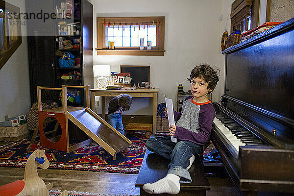 Direkter Blick auf einen kleinen Jungen  der in seinem Wohnzimmer an der Klavierbank sitzt