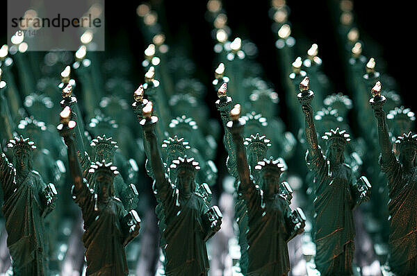 Reihen von grünen Miniaturfiguren der Freiheitsstatue mit goldenen Flammen.