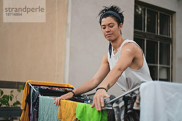 Queere asiatische Frau hängt nasse Wäsche draußen auf Kleiderständer