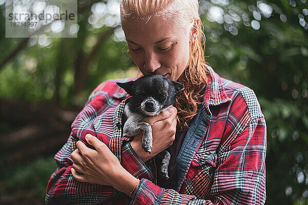 Blonde Frau hält lächelnd einen kleinen süßen Hund draußen im grünen Wald