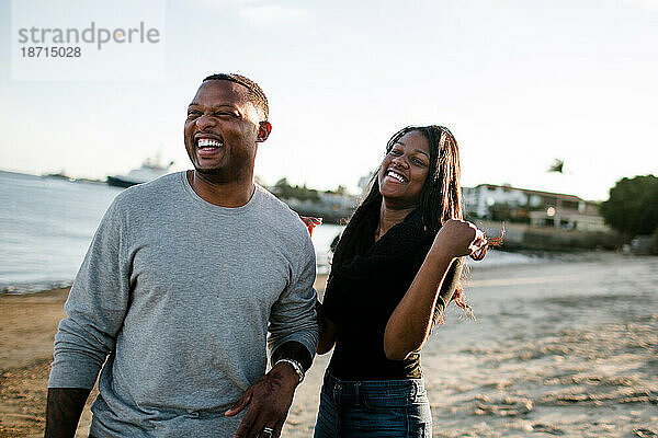 Vater und Tochter lachen gemeinsam am Strand bei Sonnenuntergang
