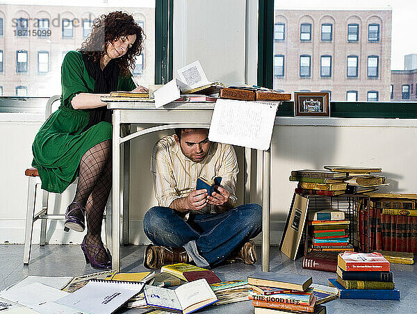 Junge Frau schreibt am Schreibtisch und ein Mann steht unter dem Schreibtisch