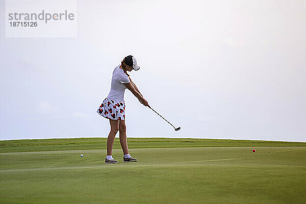 Junge Frau spielt Golf vor klarem weißen Himmel  Tanah Lot  Bali  Indonesien