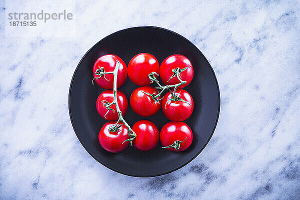 Draufsicht auf frische Tomaten auf schwarzem Teller vor Marmor