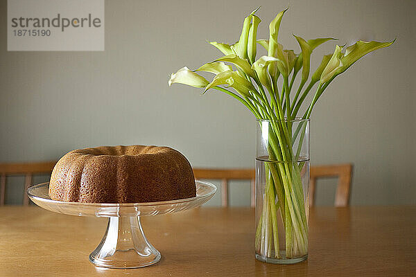 Frisch gebackener Buttermilchkuchen steht auf einem Kuchenständer neben einer Vase mit frischen Lilien in Seattle  Washington.