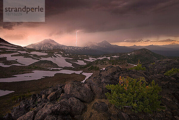 Ein dramatischer Lichtblitz ergänzt den stürmischen Himmel bei Sonnenuntergang über den Three Sisters Mountains in Oregon.
