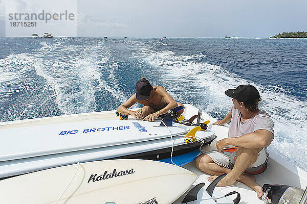 Zwei junge Männer sitzen auf einem fahrenden Motorboot und transportieren Surfbretter  Male  Malediven
