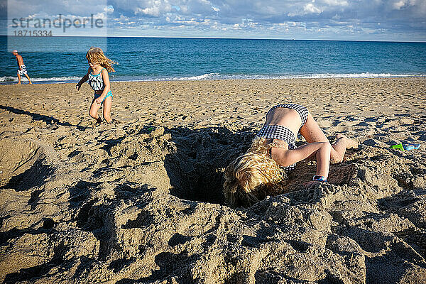 Mädchen gräbt an einem sonnigen Tag ein Loch am Strand