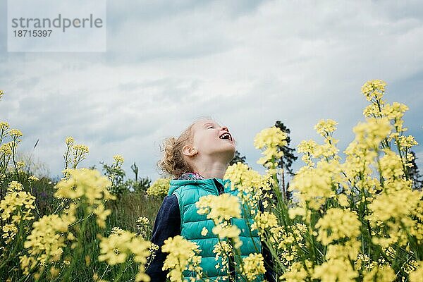 Junges Mädchen steht auf einem Blumenfeld und blickt in den Himmel