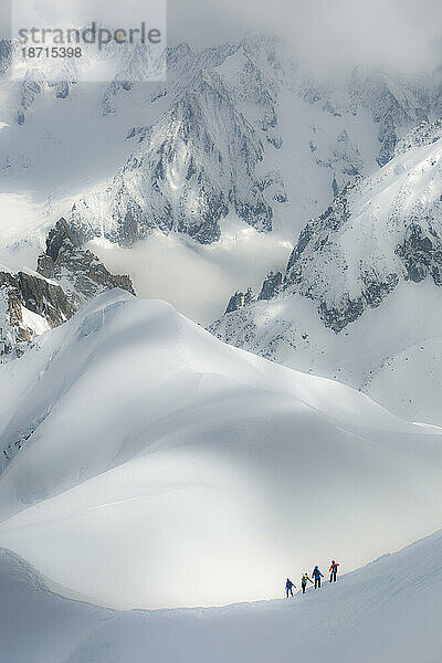 Eine Seilschaft aus vier Alpinisten steigt einen steilen Grat zwischen riesigen Gipfeln hinab