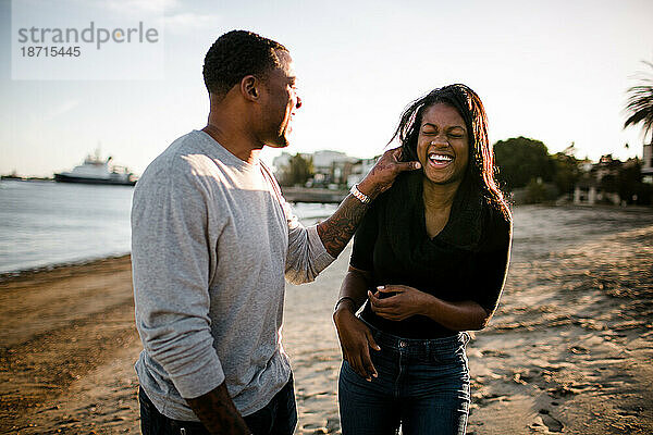 Vater und Tochter lachen und spielen bei Sonnenuntergang am Strand
