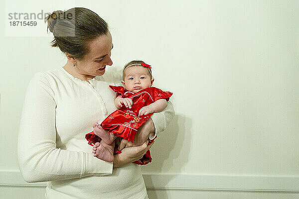 Kaukasische Mutter hält Tochter in traditioneller roter chinesischer Kleidung