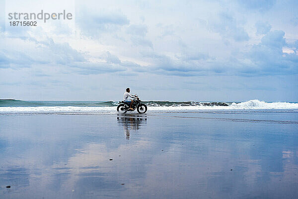 Mann fährt mit Motorrad am Meeresstrand.