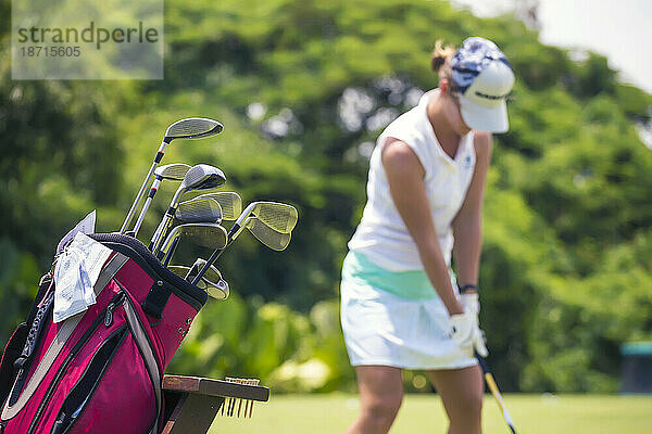 Golftasche und junge Frau spielen Golf im Hintergrund