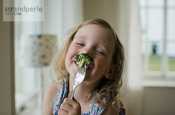 Junges Mädchen lacht mit unordentlichem Gesicht  während es Brokkoli isst