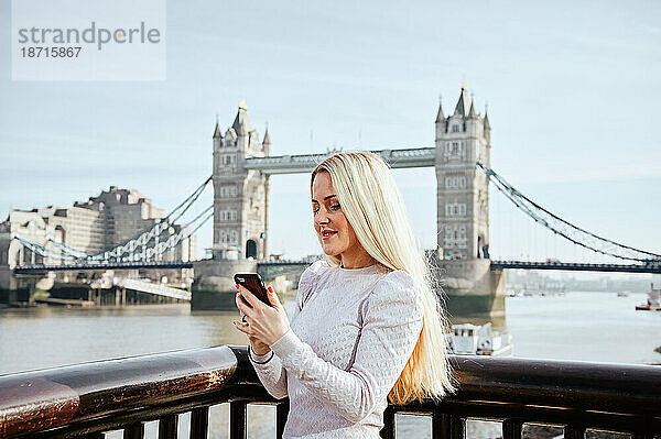 Attraktive Frau blickt auf ihr Mobiltelefon vor dem Hintergrund der Tower Bridge