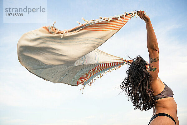 Latina-Frau vergnügt sich am Strand mit Handtuch im Wind