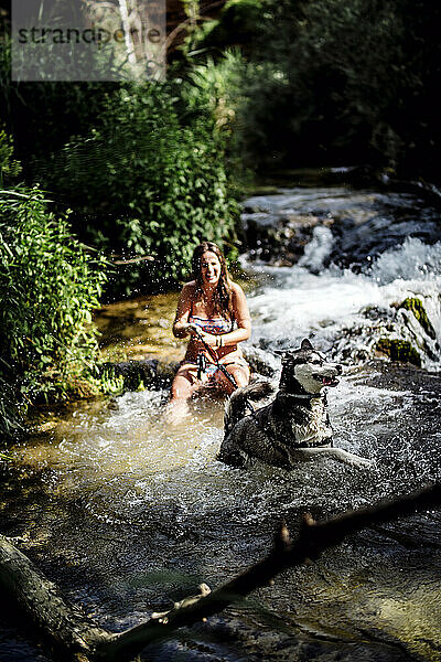 Blonde Frau badet in einem schönen Fluss mit einem Siberian Husky-Hund.