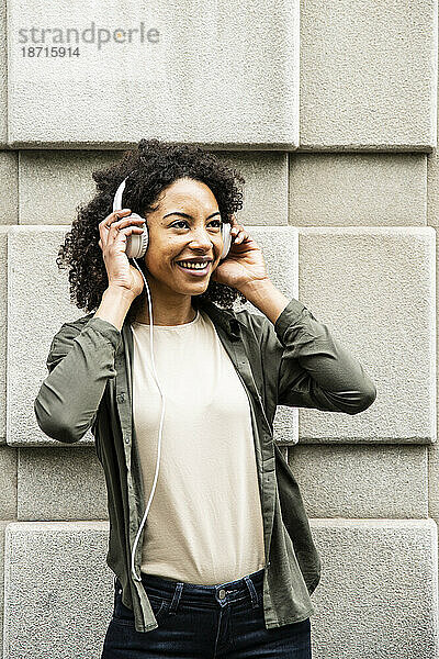 Junge Frau lächelt  während sie auf der Straße Kopfhörer benutzt.