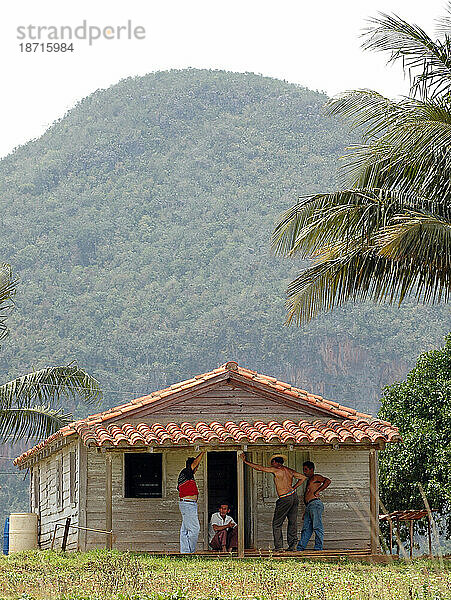 Männer hängen auf der Veranda eines kleinen Holzhauses im ländlichen Kuba herum.