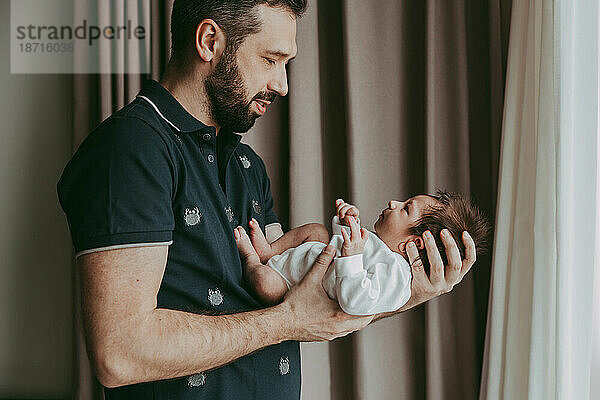 Papa hält seinen neugeborenen Sohn im Arm und schaut ihm in die Augen