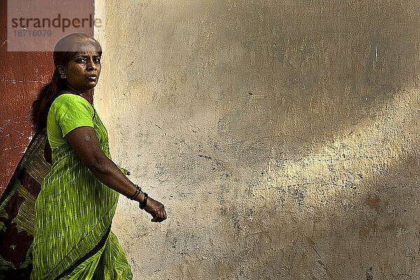 Eine Frau mittleren Alters in einem grünen Sari geht an einer rot-weißen Wand vorbei.
