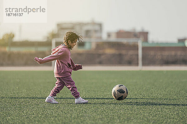 Sportkind. Glückliches kleines Mädchen  das einen Fußball tritt  Kind spielt