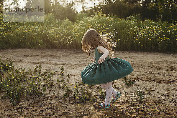 Kleines Mädchen dreht ihr Kleid im Gegenlicht und in einer Blumenwiese