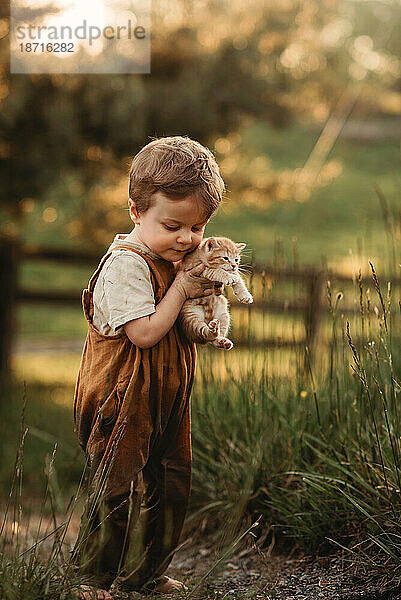 Kleinkind hält ein Kätzchen  das draußen auf einem Bauernhof kuschelt