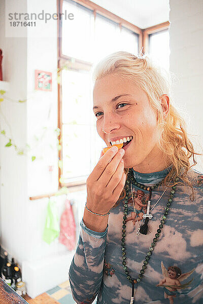 Helles Porträt einer schönen blonden queeren Frau  die zu Hause Obst isst